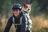 Woman biking with a dog in a Ruffwear Hitch Hiker Dog Backpack Carrier, enjoying outdoor adventures.